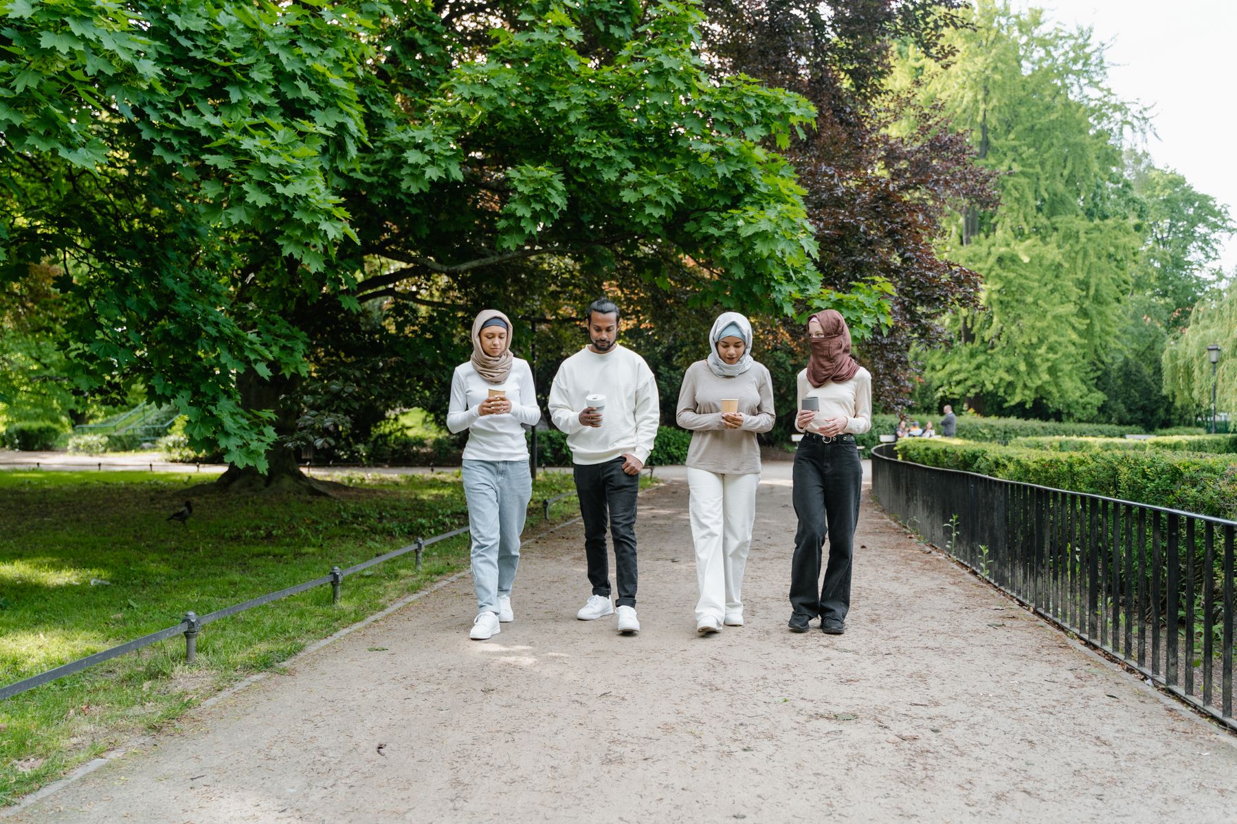 Four adults walk together along a green park path.